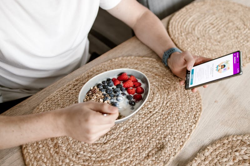 Man met gezond ontbijt aan tafel en mobiel in hand