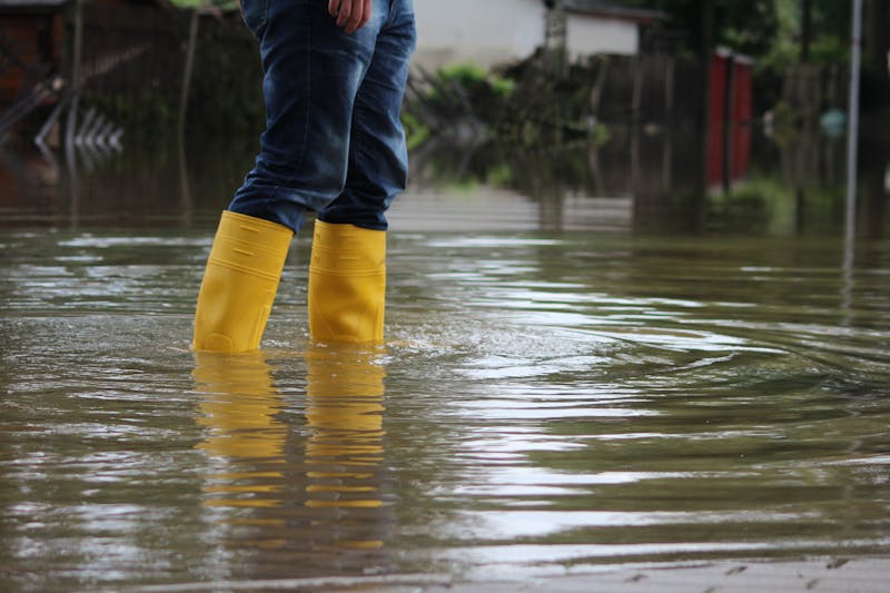 Een persoon staat met regenlaarzen in hoog water