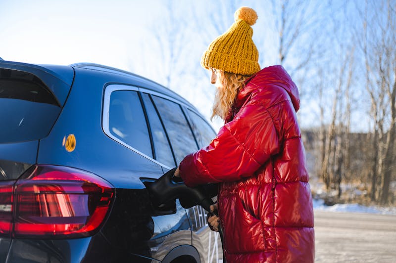 Vrouw laadt elektrische auto op in de winter