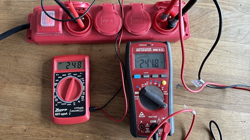 Multimeters aangesloten op netspanning, links bouwmarkt-budget-exemplaar en rechts professionele meter.