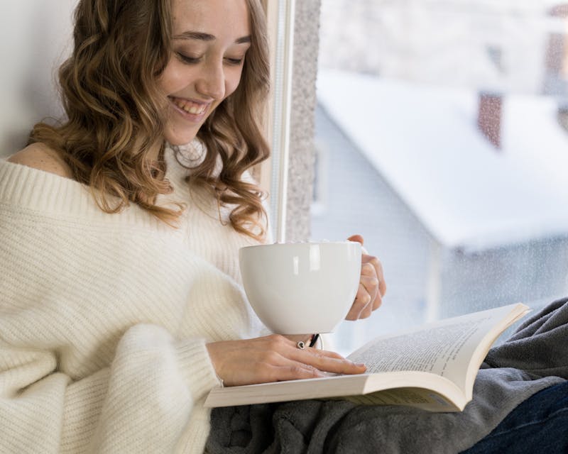 Meisje dat bij het raam zit te lezen