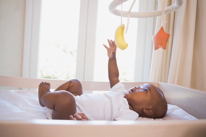 Baby ligt in de box en speelt met een mobile