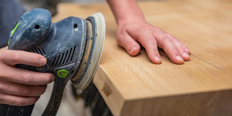 Iemand schuurt een plank met een schuurmachine