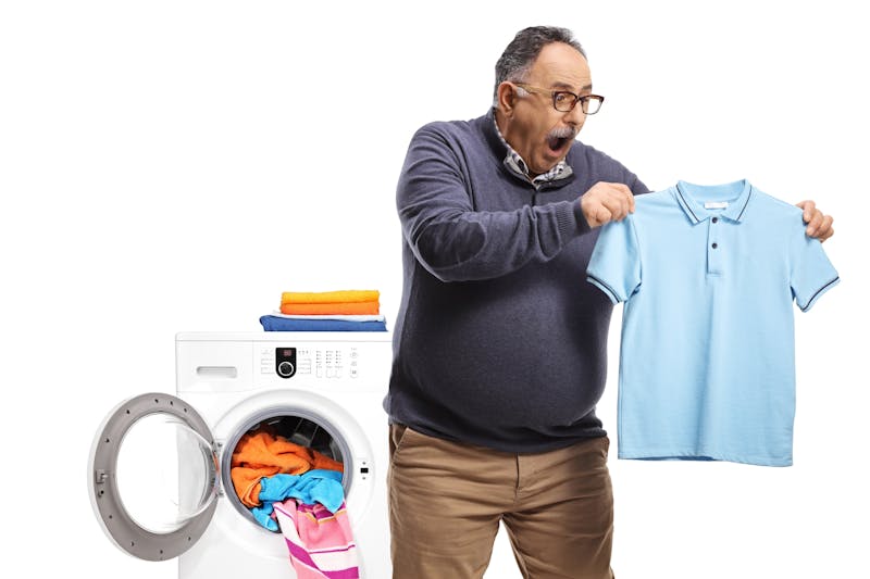 Man die blauwe polo uit de wasmachine haalt en geschrokken kijkt alsof de polo gekrompen is