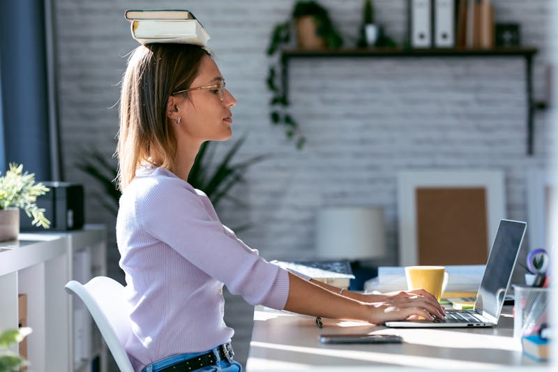 Vrouw balanceert boek op haar hoofd achter haar bureau