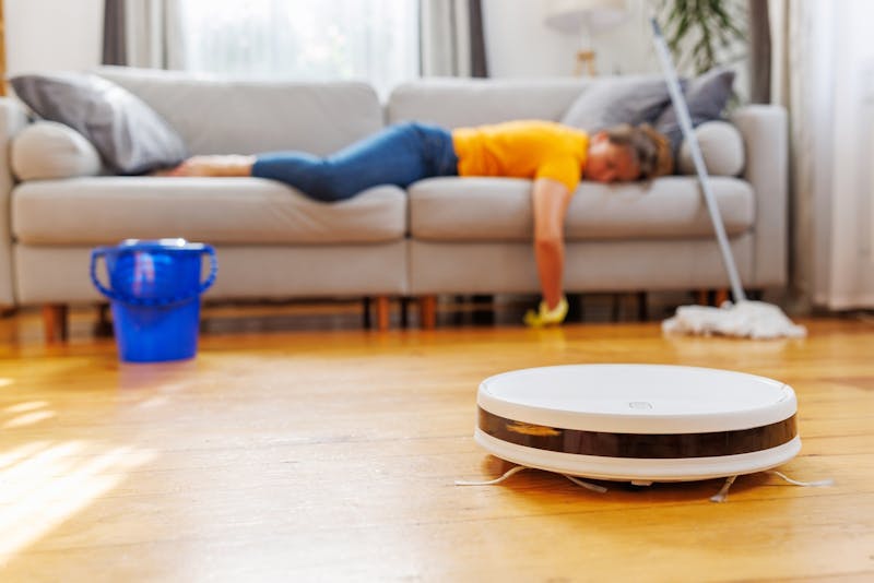 Vrouw ligt op de bank terwijl de robotzuiger het werk doet