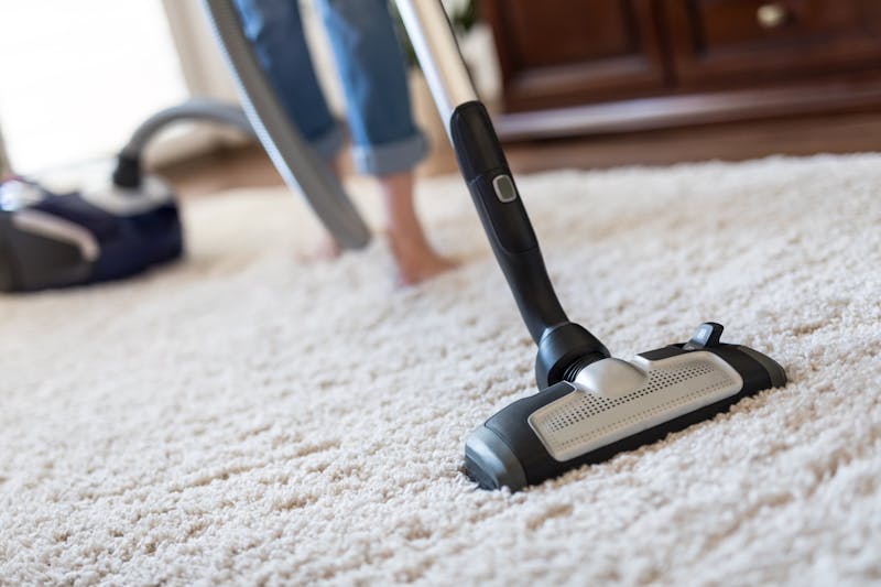 Een vrouw die met een steelstofzuiger een hoogpolig tapijt stofzuigt