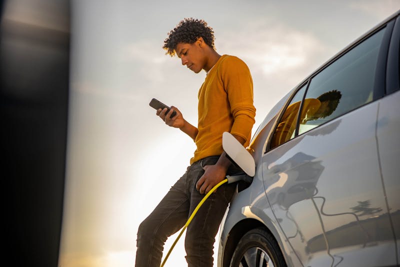 Man die naast een elektrische auto staat die aan een oplaadpaal hangt