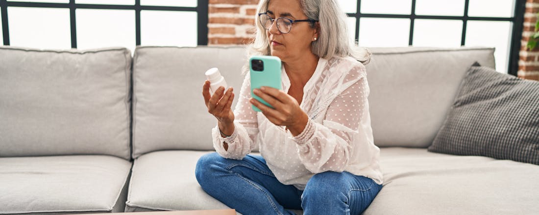 vrouw met medicijnpotje en smartphone Geheugentrainer: zo houd je je geheugen op peil