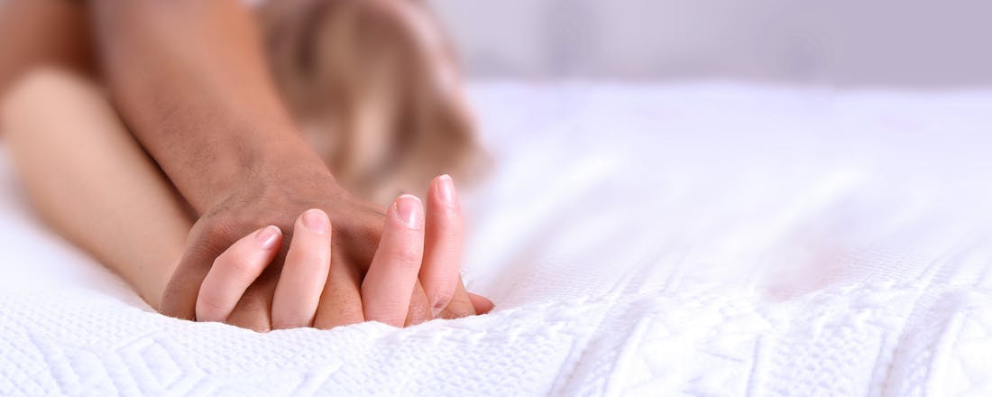 Man en vrouw in bed met verstrengelde handen liefde intimiteit Je seksuele gezondheid: dit is waarom je daar tijd voor moet maken