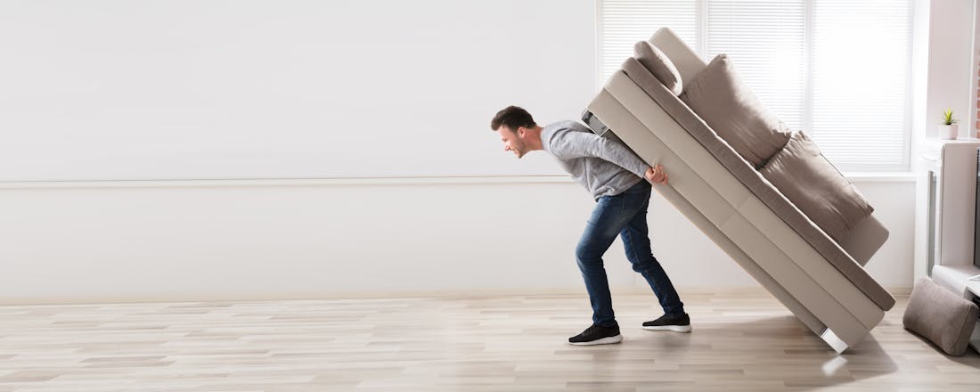 Man die sofa op zijn rug door kamer sleept.Langwerpig beeld, header Zo voelt je huis weer als nieuw: tips en trucs voor een nieuwe indeling
