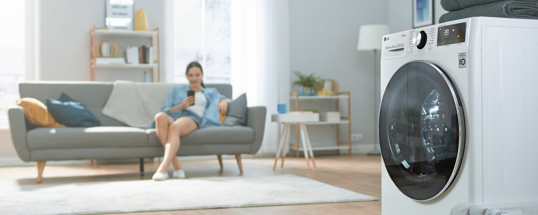 vrouw die kijkt naar telefoon met wasmachine op achtergrond Slimmer wassen: koud is het nieuwe warm