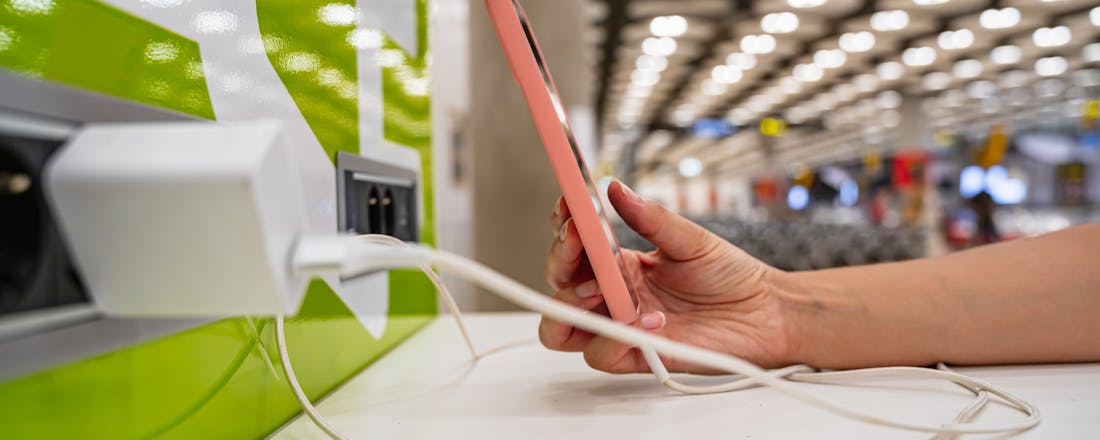 iemand die een smartphone oplaadt bij een openbaar oplaadpunt Openbaar oplaadpunt? Pas op, je smartphone kan gehackt worden!