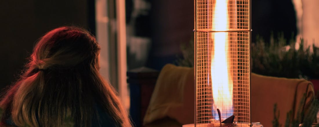 Vrouw zit bij terrasverwarmer Langer buiten zitten met terrasverwarming: keuzehulp