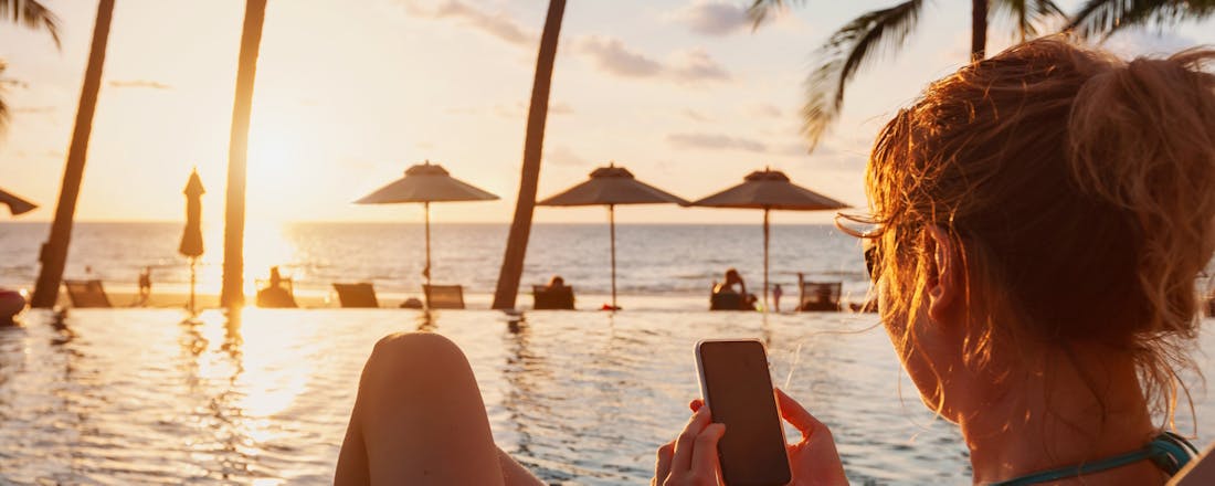 Vrouw zit met smartphone op vakantie bij een zwembad Een goede voorbereiding is het halve werk: stabiel internet op vakantie