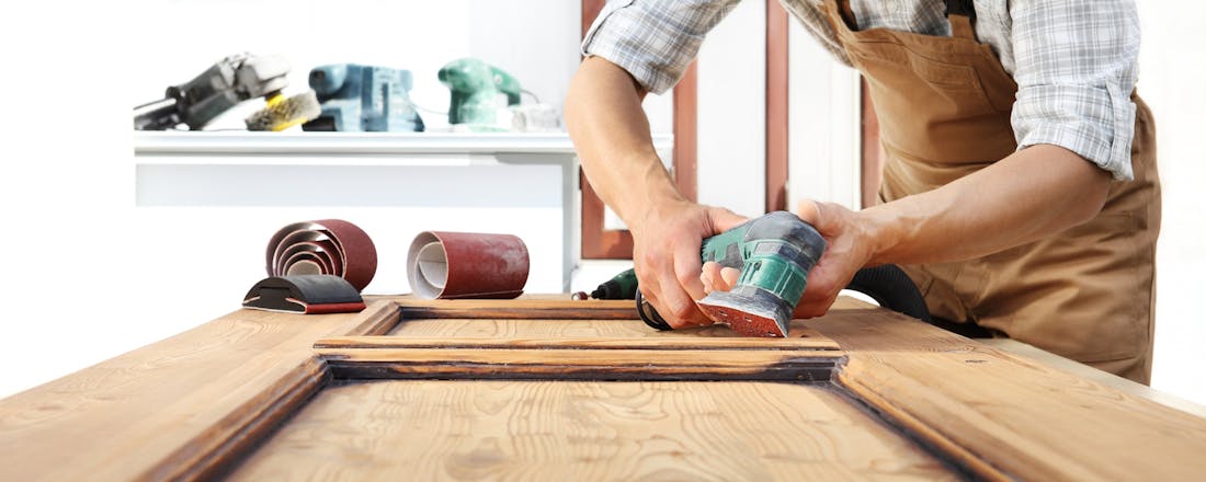 Man is aan het schuren met een schuurmachine Een deur schuren: een handleiding met praktische tips