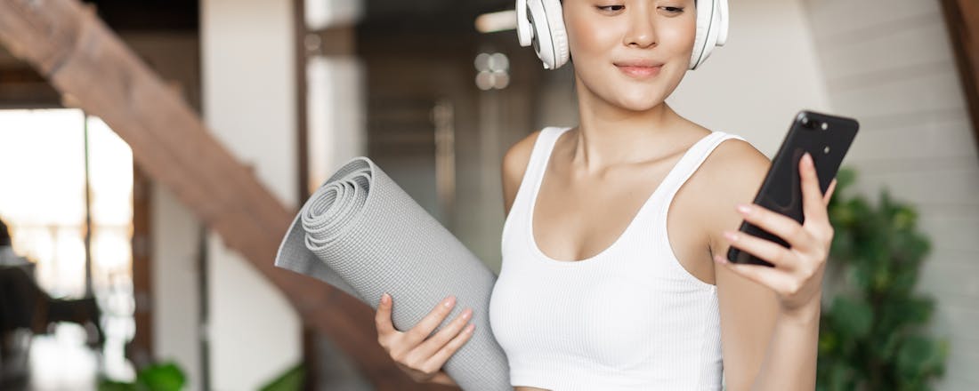 Vrouw met yogamatje en koptelefoon Muziek tijdens het sporten: do’s en don’ts