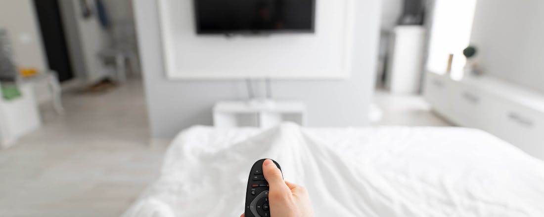 Man met afstandsbediening in bed 📺 Tv in de slaapkamer? Met deze tips plaats je 'm perfect