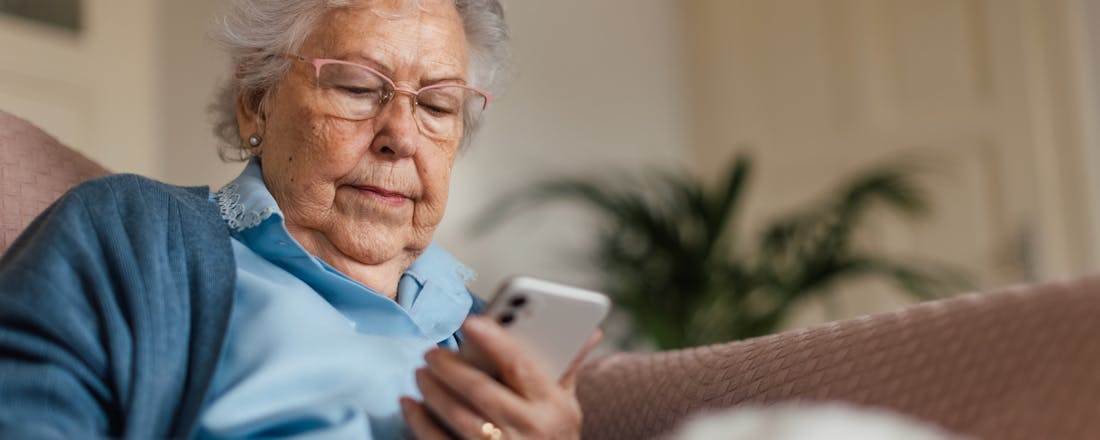 Oudere dame kijkt op haar smartphone 4 manieren waarop wearables oudere mensen helpen